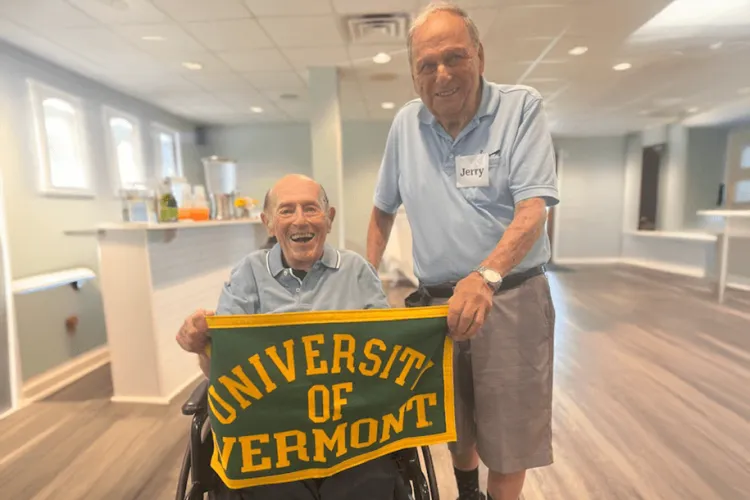 Two men smiling holding a University of Vermont flag. 