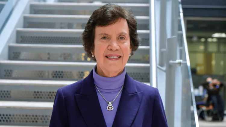 Woman in a purple turtleneck and blazer smiles on the stairs.