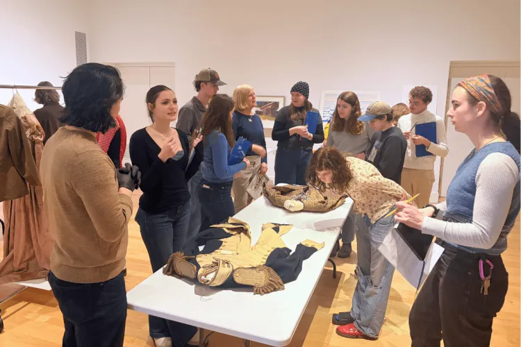 A class of students looking closely at clothing on display.