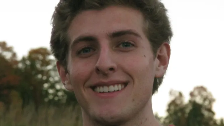 Close-up of a smiling person with trees blurred in the background.