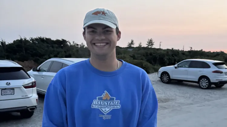 Person smiling outdoors at sunset with parked cars and trees in the background.
