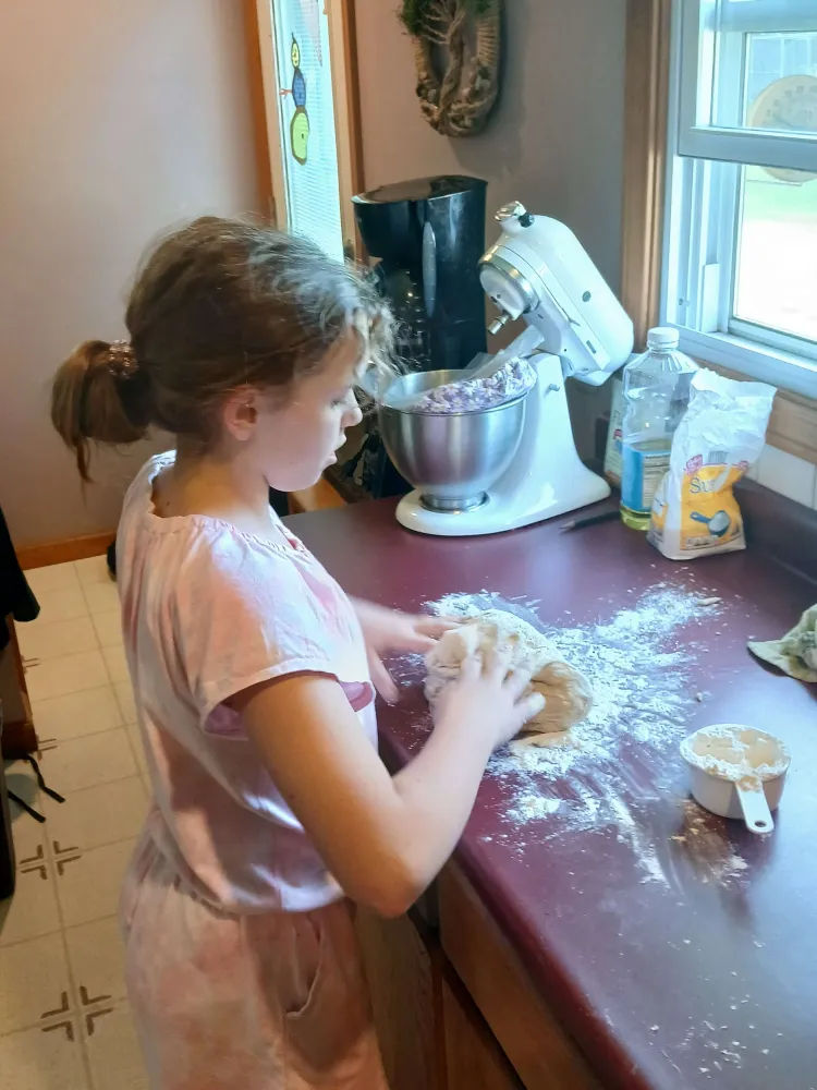 A young person at a kitchen counter with their hands on bread dough