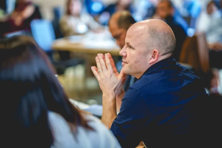 Person looks out into a conference with hands pressed together