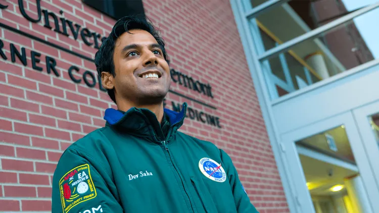 a person in a green NASA jacket standing outside the Larner College of Medicine
