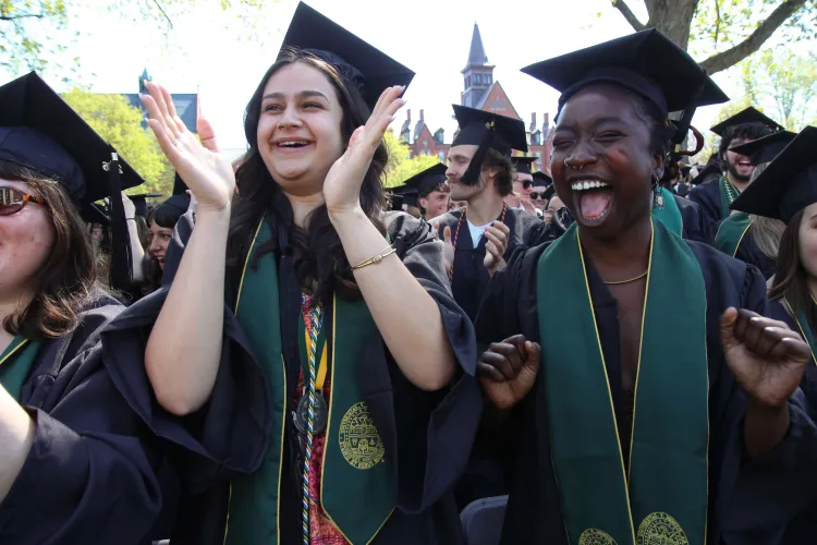 People in caps and gowns and green sashes cheer and clap