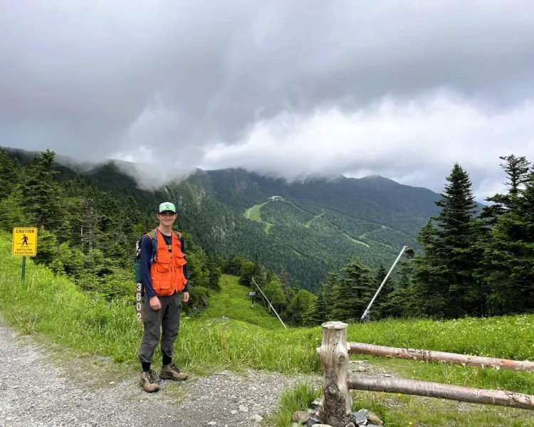 Christian Baker standing on a gravel path with a forested mountain in the background