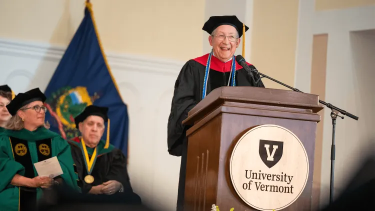 a person wearing regalia at a podium with people in regalia looking on