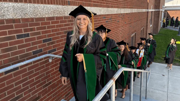 a line of graduating students in academic regalia coming up a stairway outdoors