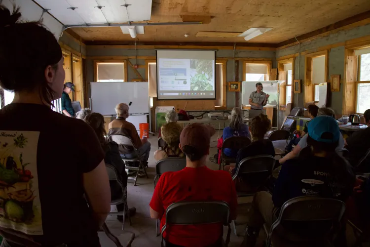 A group of people in a room with windows and a screen up front. 