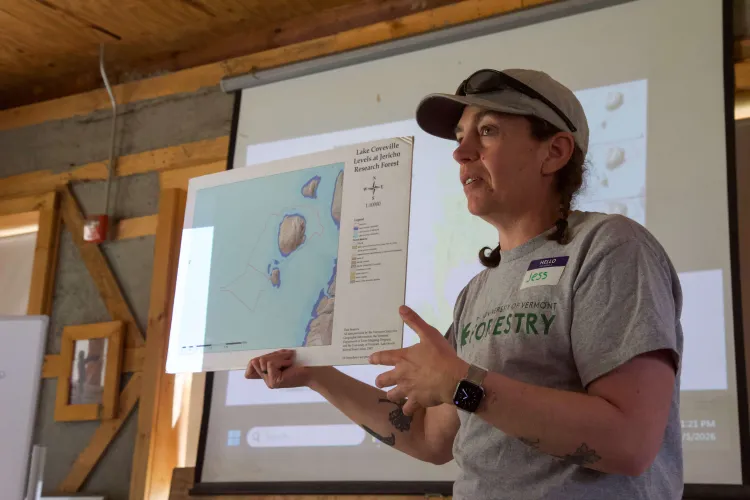 A woman holds up a small poster showing water covering a region with some small islands of land poking up. 