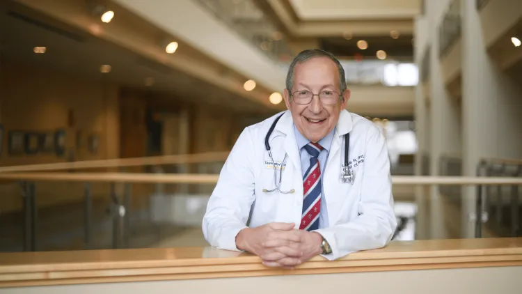 a smiling doctor in a white coat standing at a railing