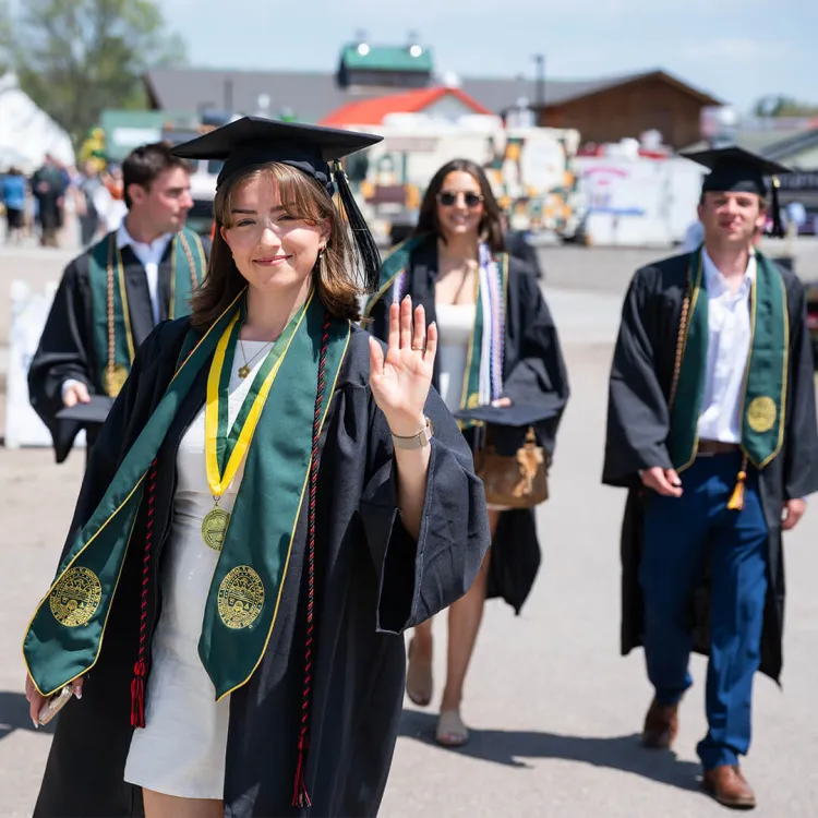 Students in caps and gowns walk outside to the commencement ceremony.