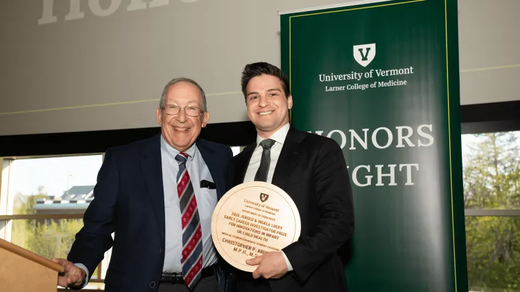 2 people posing with an award plaque in front of an Honors Nighht banner
