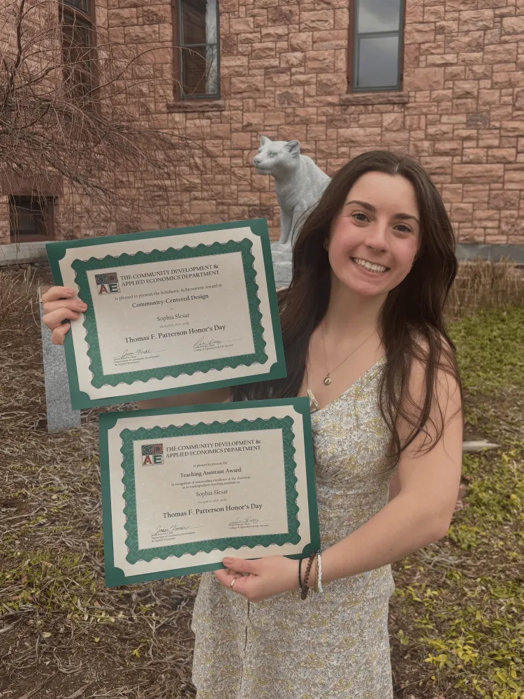 A young woman holding up two award certificates