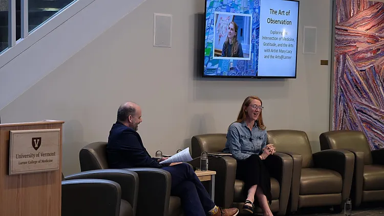 2 people speaking with a screen in the background