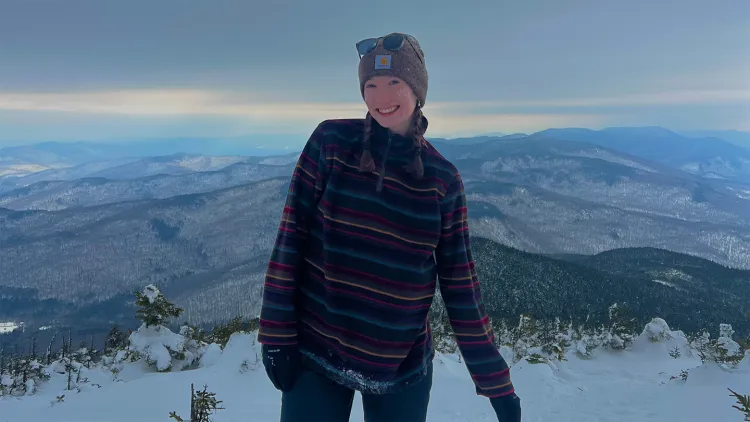 Young woman with winter hat and striped fleece pullover smiling on snowy mountaintop