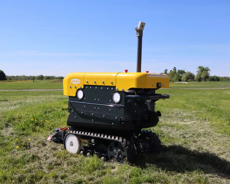 A yellow, boxy robot on treads in a grassy field against a blue sky.