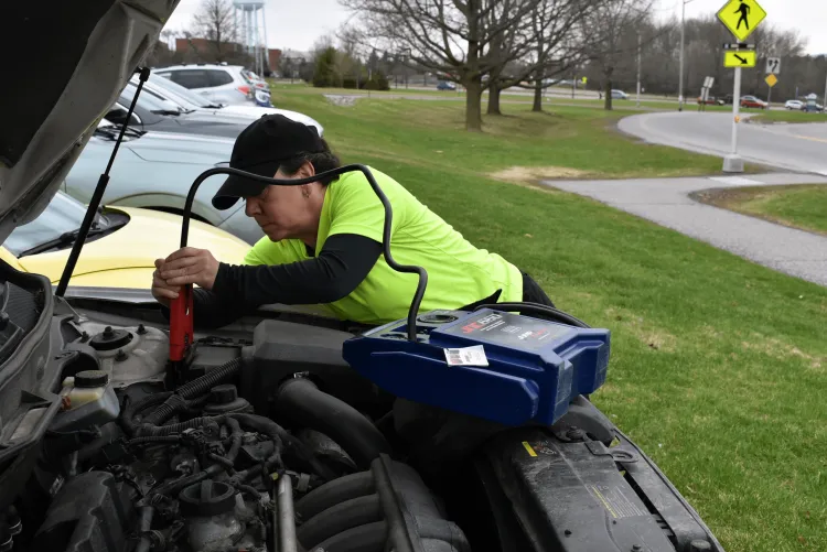A UVM parking officer attaching jumper cables to a student's car battery