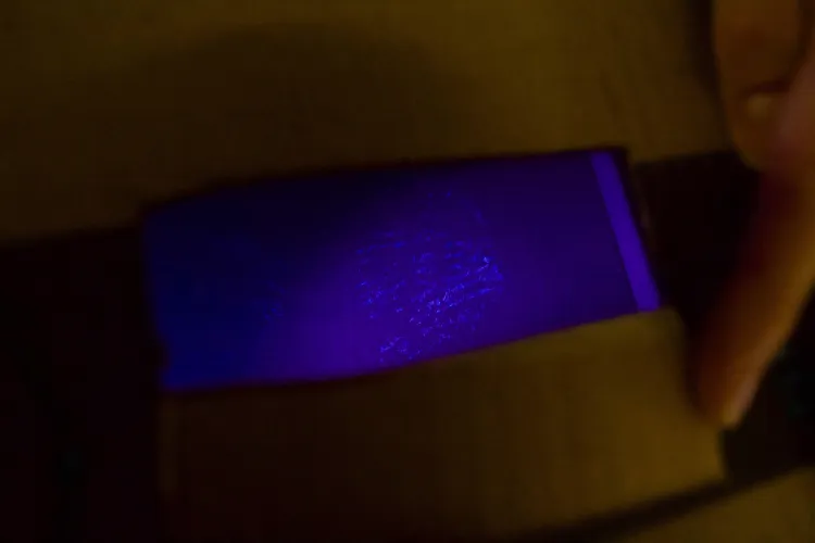 A hand around a cut-out rectangle in a cardboard box that shows a footprint in a purple-blue light.