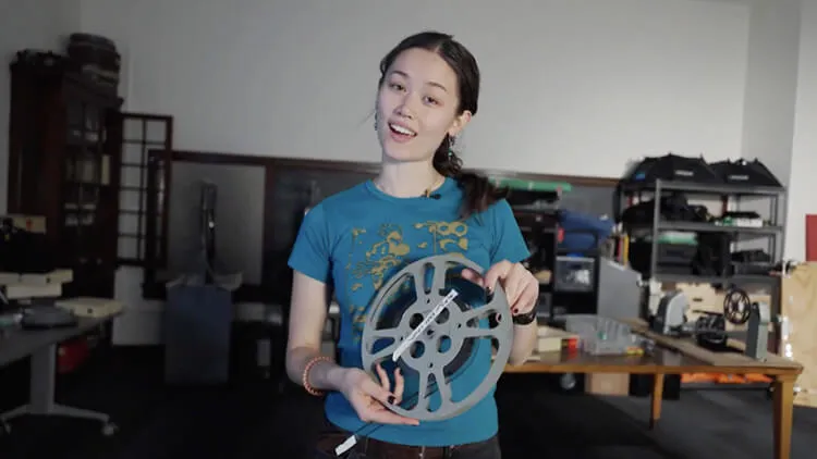 A woman holding a large film reel in a workshop or studio space.