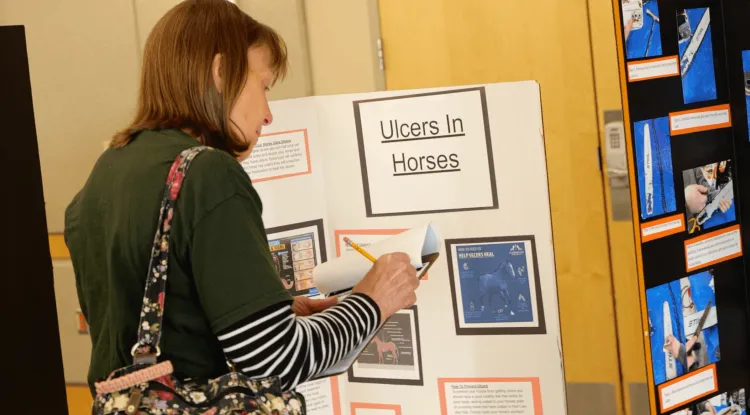 A person stands in front of a poster that reads "ulcers in horses."