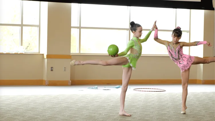Two young people in bright pink and green leotards dance with a green ball