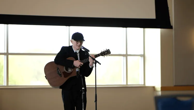 A young person holds a guitar in front of a microphone