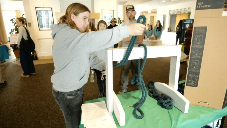 A young person pulls a rope around a white-painted panel of wood, tying it in a knot for people.