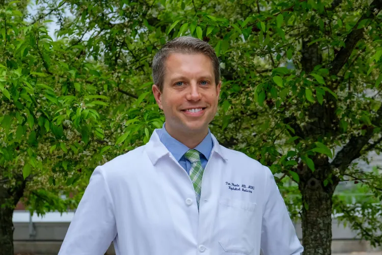Person in lab coat in front of trees outside. 