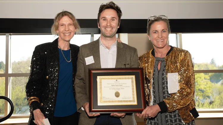 a person holding an award, flanked by 2 people