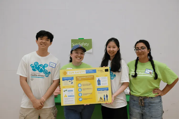 Four people smiling at the camera inside holding a signboard. 