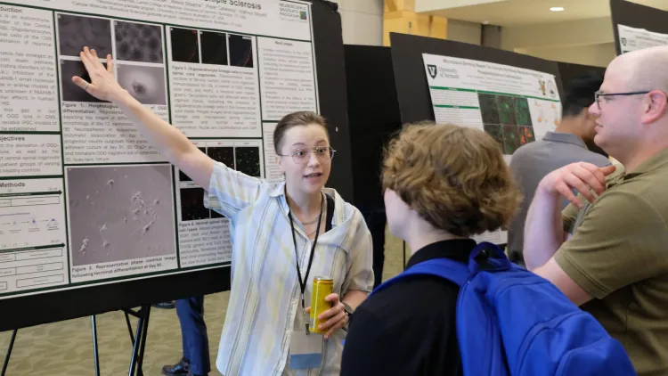 a person describing their poster at a research symposium