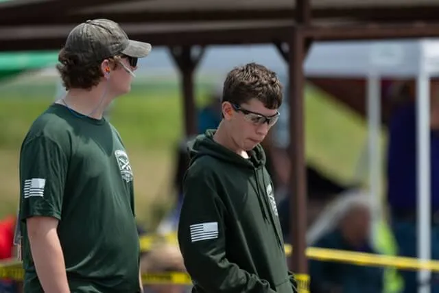 Two young people in green tops and safety glasses stand outside on a sunny day.