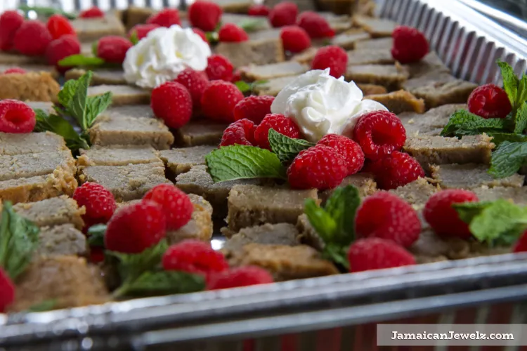 A tray full of brown pudding cake with raspberries, mint leaves and little bits of whipped cream on top.