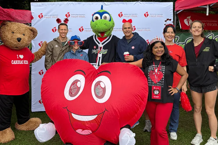 A group of people and three mascots, one a bear, the other a heart, and the third Champy the Lake Monster,  all in a group photo smiling at the camera. 