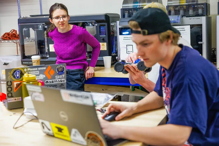 A faculty member works with students at a laptop in a laboratory
