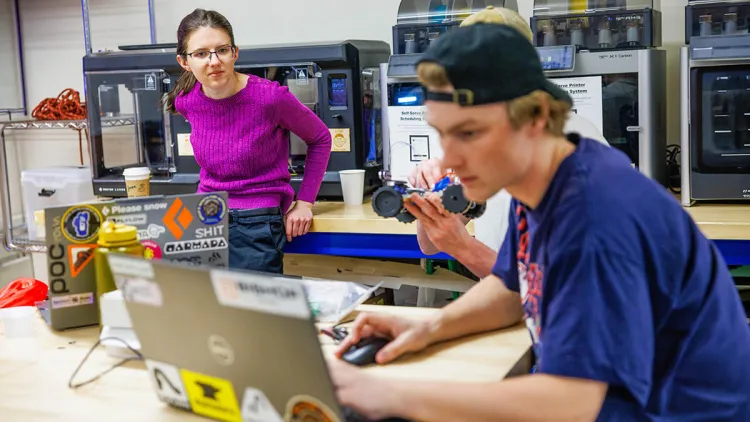 A student works on his laptop in a lab while the instructor looks on