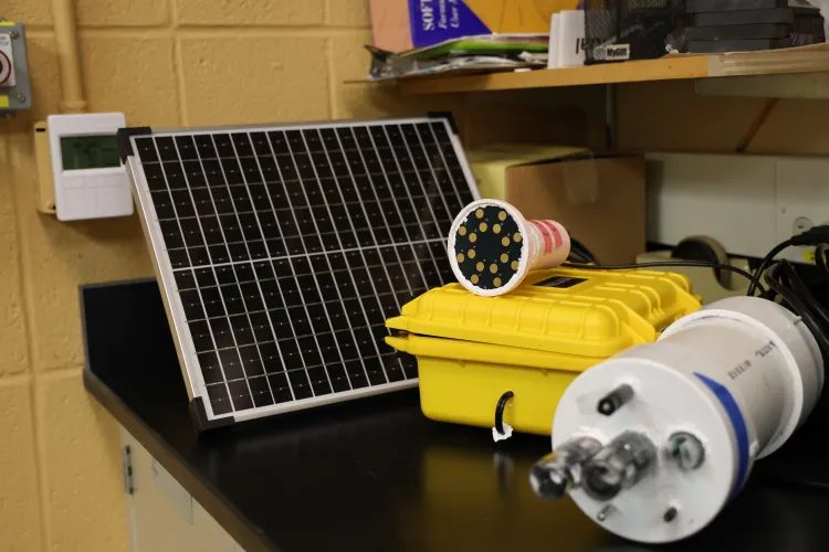 A small gadget sitting on a yellow case next to a solar panel. 
