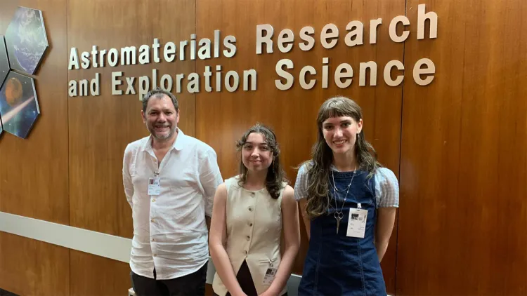 Three people stand in front of wall under sign that says "Astromaterials Research and Exploration Science"