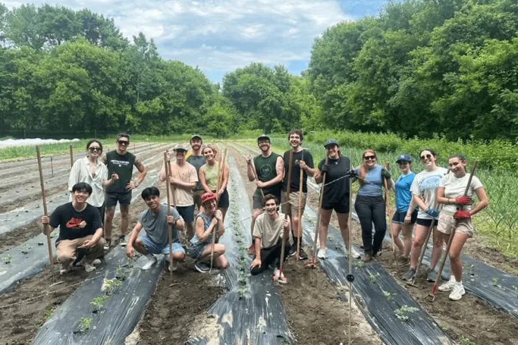 A group of students outside on a farm smiling at the camera together. 