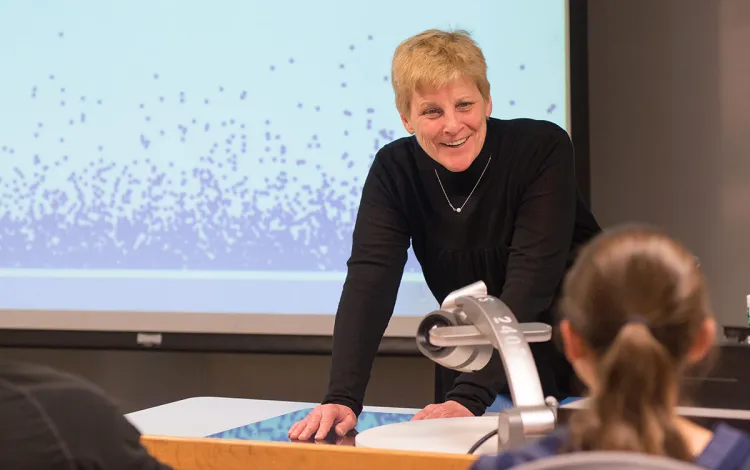 A faculty member discusses a lesson with students with a screen in the background