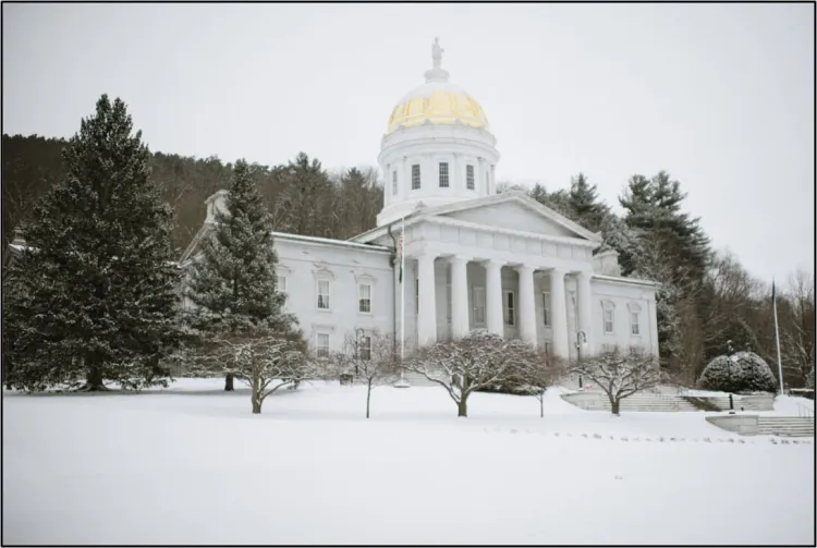 Photograph of the Vermont state capital building, surrounded by snow-covered ground and trees. 