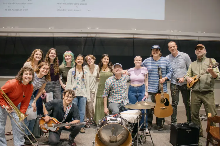 A group of students pose for a photo with their professors while holding instruments.