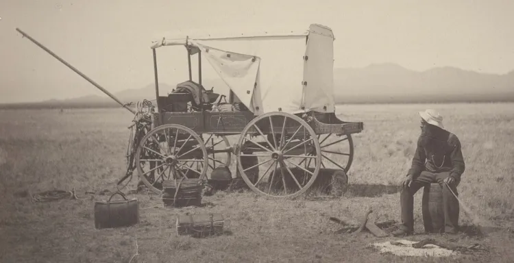 Cyrus Pringle alone at his desert camp, sitting next to his wagon