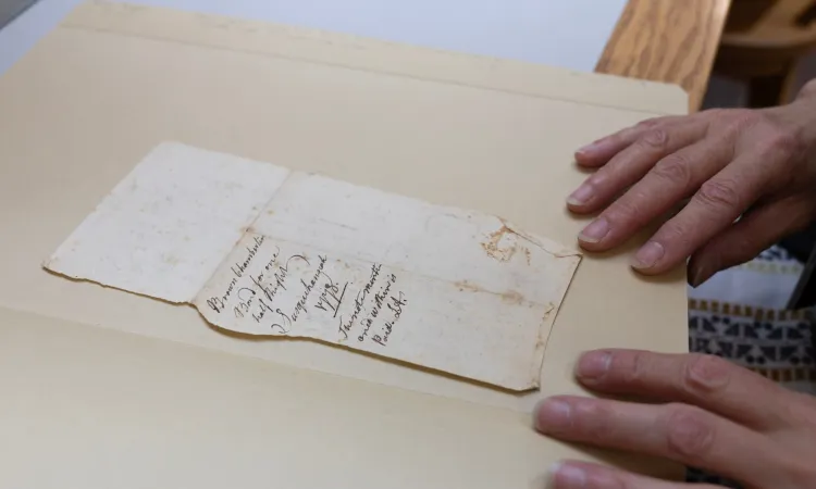 Hands next to an old, weathered document with cursive writing.