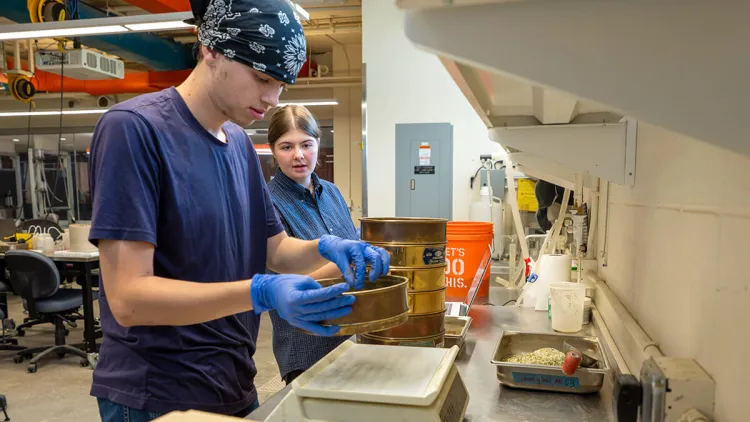 Two students working at a lab table taking samples and entering the results into a laptop