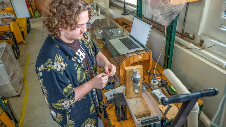 A student conducts research using lab equipment with his laptop nearby