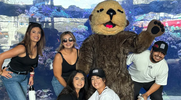 a group of people posing with a sea otter mascot at an aquarium