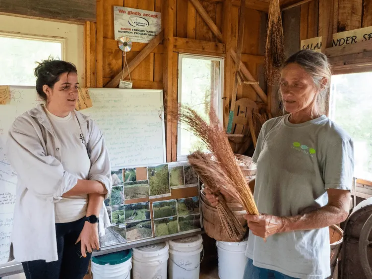 Two people stand in a farm stand, one holds grain from a field
