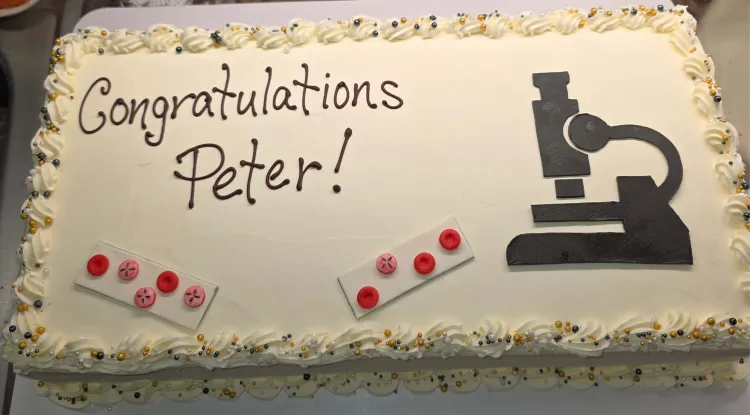a celebratory sheet cake decorated with a microscope, slides with candy blood drops adorned with babesia, and the words "Congratulations Peter!"